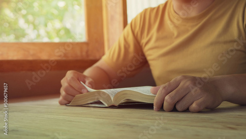 A man holding and read book on wood table with window light, crisis solution pray to God, Christian believe, trust and obey , morning devotional concept with copy space