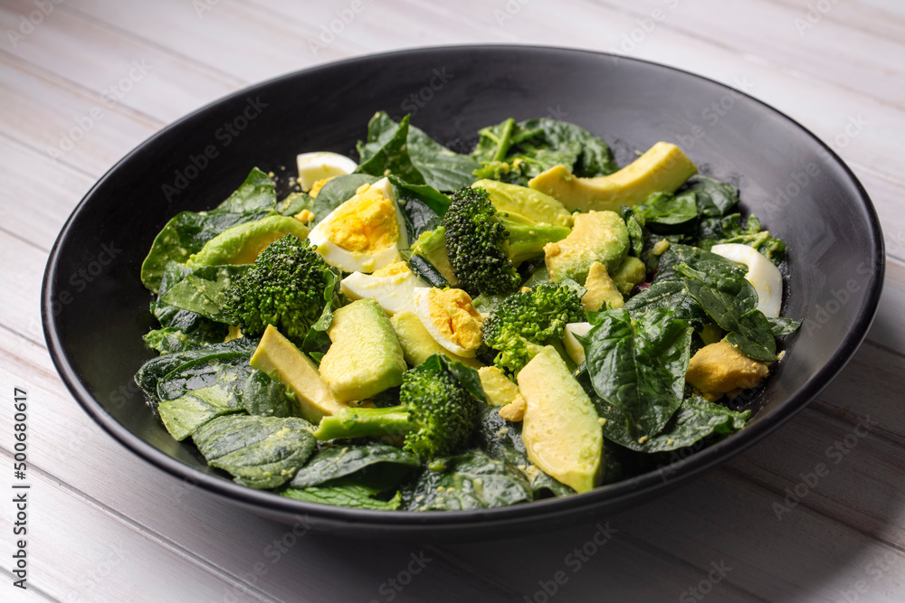 Avocado salad with broccoli, boiled egg in white vintage bowl on light salad Avocado salad with broccoli, boiled egg in white vintage bowl on light salad