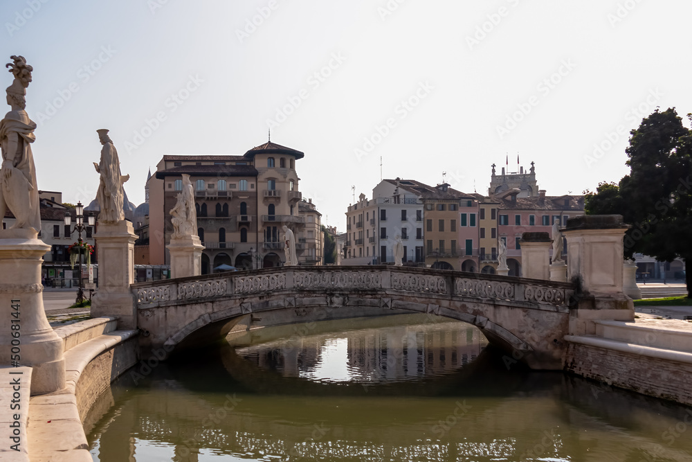 Scenic view on bridge of Prato della Valle, square in the city of Padua, Veneto, Italy, Europe. Green island at center, Isola Memmia surrounded by canal bordered by two rings of statues. Reflection