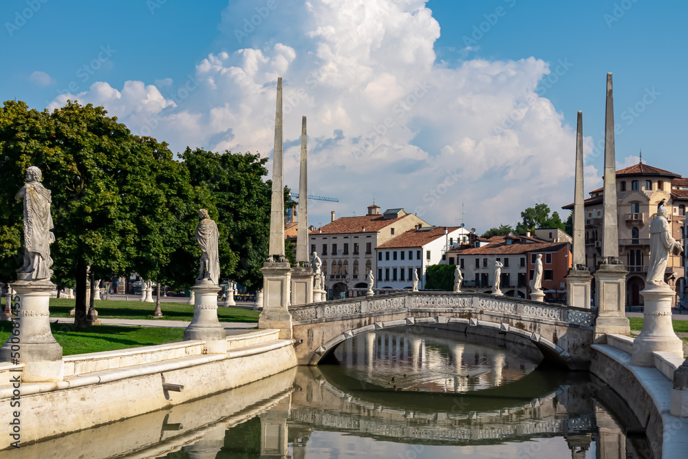 Scenic view on bridge of Prato della Valle, square in the city of Padua, Veneto, Italy, Europe. Green island at center, Isola Memmia surrounded by canal bordered by two rings of statues. Thick clouds