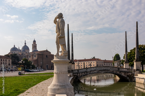 Scenic view on bridge of Prato della Valle, square in city of Padua, Veneto, Italy, Europe. Close up on statue of Galileo Galilei. Isola Memmia surrounded by canal bordered by two rings of statues