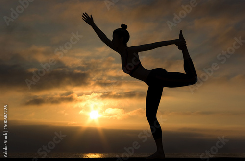 Woman side silhouette in Yoga Dancer pose at sunset with Cloudy sky and quiet sea