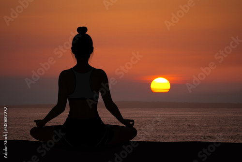 Woman silhouette in Yoga Easy Meditating pose at sunset with quiet ocean