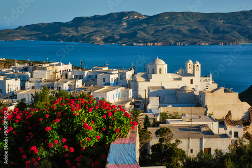 Picturesque scenic view of Greek town Plaka on Milos island over red geranium flowers. Plaka village, Milos island, Greece