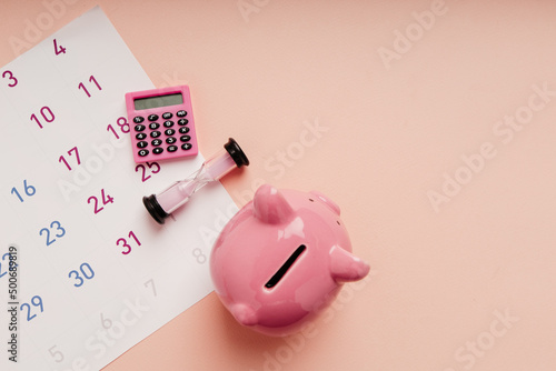 Top view of piggy bank, hourglass and calculator on calendar's sheets. Tax, afinancial goal, money saving concept photo