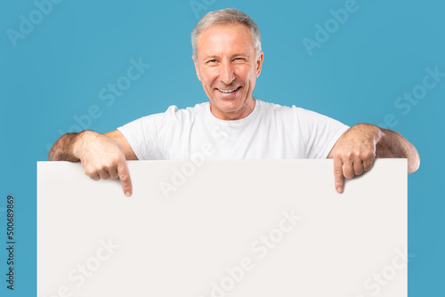 Mature man peeking out blank white advertising billboard at studio