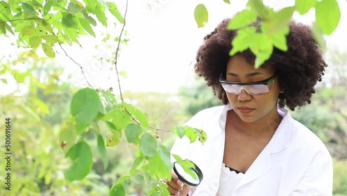 Beautiful woman teaching young kid examining green leaf through a magnifying glass in the garden. Concept of self learning in springtime.