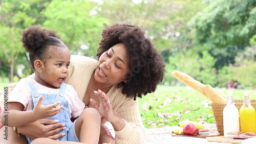Beautiful mother teach and introduced quality of red apple to daughter while relax and picnic in public park. Summertime in the last weekend.