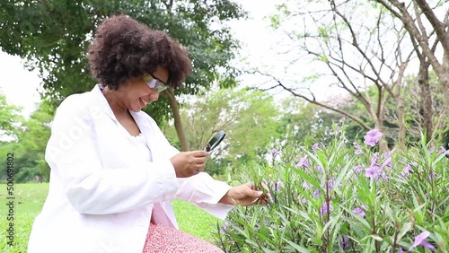 Portrait of beautiful young scientist holds a magnifying glass to use to explore and find flowers and plant species for agronomic research. Science and Technology concept in the forest