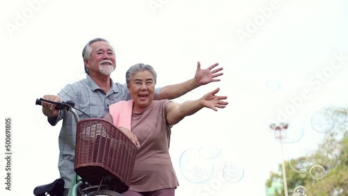 An elderly couple enjoys cycling and relaxing in the park with bright smiles and enjoys relaxing after retirement. Healthy and insurance concept