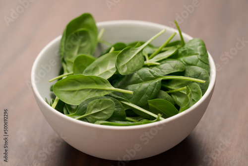 Fresh spinach leaves in white bowl on walnut wood table