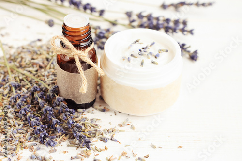 Lavender essential oil herbal extract in glass bottle with skincare moisturizer cream cosmetic container, dried purple blossom white table closeup