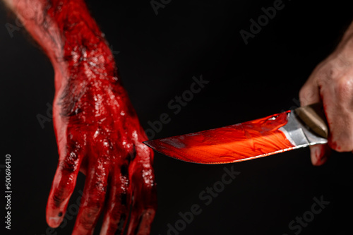 Man holding knife with bloody hand on black background. 