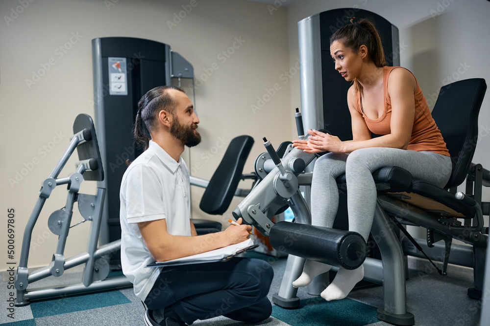 Fototapeta premium Athletic woman and her fitness instructor talk while making exercise plans in a gym.