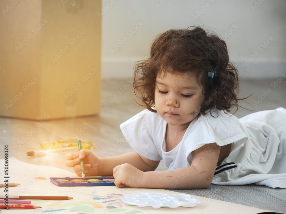 Cute little toddler girl lying down on the floor drawing and painting on brown paper. Cute little toddler girl lying down on the floor drawing and painting on brown paper.