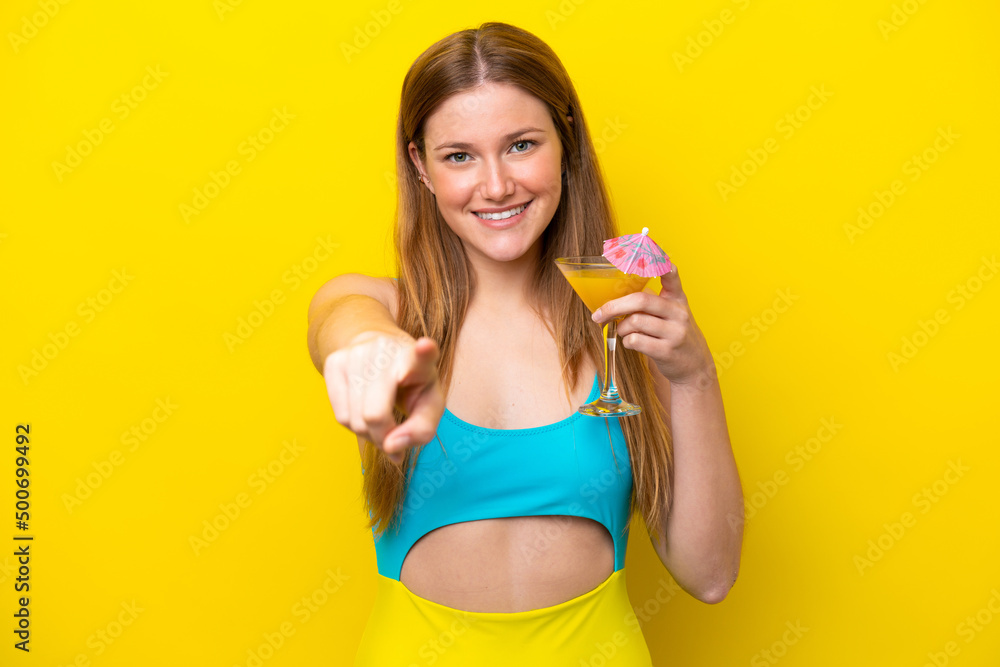 Young caucasian woman holding a cocktail isolated on yellow background points finger at you with a confident expression Young caucasian woman holding a cocktail isolated on yellow background points finger at you with a confident expression