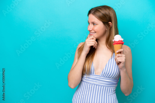 Young caucasian woman in swimsuit eating ice cream isolated on blue background thinking an idea and looking side