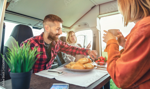 Happy friends having breakfast in a camper van in the morning