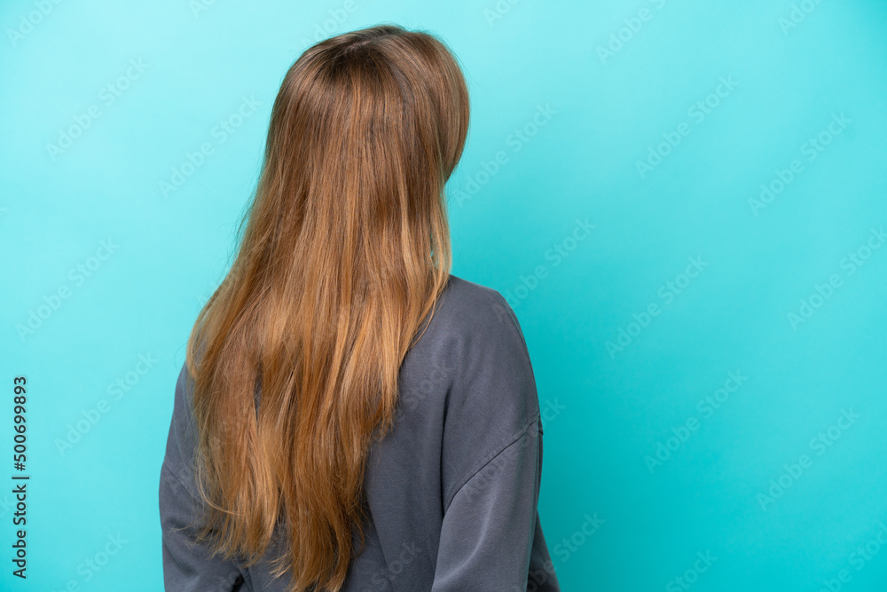 Naklejka premium Young caucasian woman isolated on blue background in back position and looking back