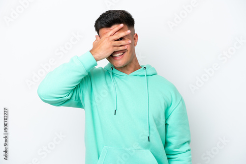 Young caucasian handsome man isolated on white background covering eyes by hands and smiling © luismolinero