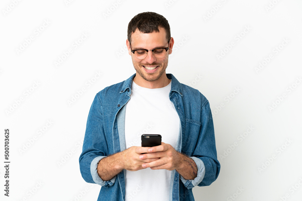 Brazilian man over isolated white background sending a message with the mobile Brazilian man over isolated white background sending a message with the mobile