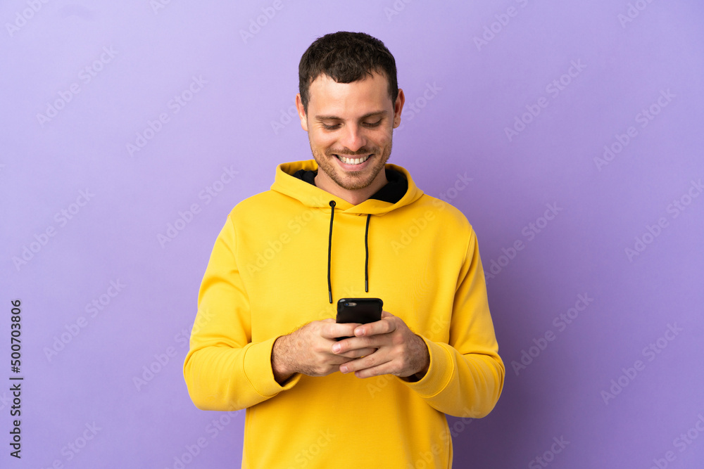 Brazilian man over isolated purple background sending a message with the mobile Brazilian man over isolated purple background sending a message with the mobile