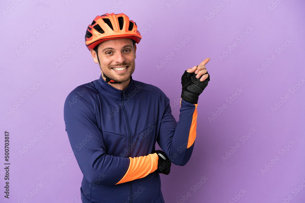 Young Brazilian cyclist man isolated on purple background pointing finger to the side - obrazy, fototapety, plakaty 