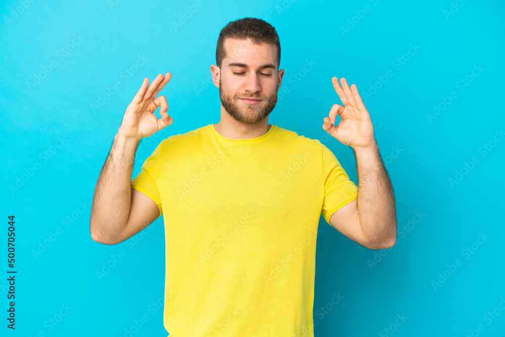 Young handsome caucasian man isolated on blue background in zen pose Young handsome caucasian man isolated on blue background in zen pose