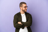 Young handsome caucasian man isolated on purple background looking to the side