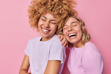 Happy pretty women laugh positively express happy sincere emotions have friendly relationship spend free time together stands closely dressed in casual t shirt isolated over pink background.