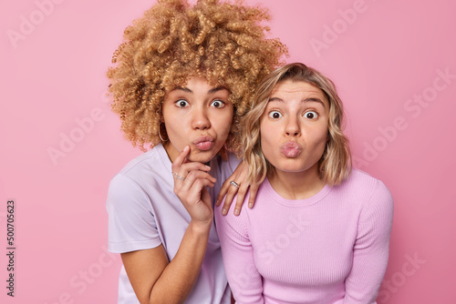 Human facial expressions concept. Surprised young beautiful women stare at camera keep lips folded react on amazing news dressed in casual clothes isolated over pink background admire something