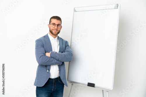 Young handsome caucasian man isolated on white background with arms crossed while giving a presentation on white board © luismolinero