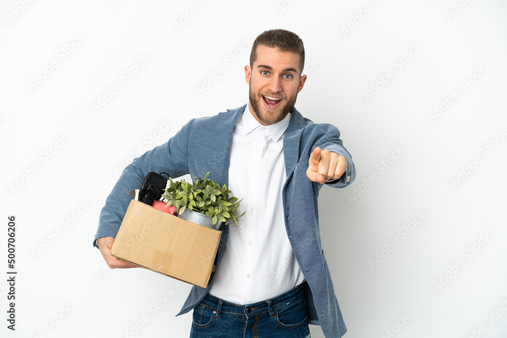 Young caucasian making a move while picking up a box full of things isolated on white background surprised and pointing front Young caucasian making a move while picking up a box full of things isolated on white background surprised and pointing front
