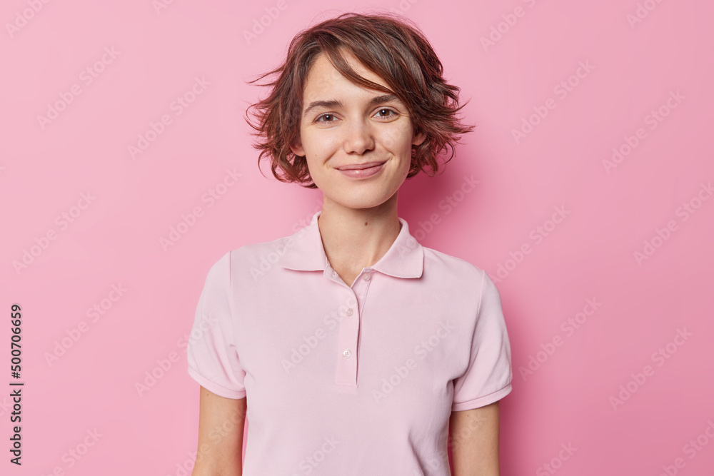Portrait of good looking brunette woman smiles tenderly has charming look wears casual t shirt looks satisfied at camera isolated over pink studioo background receives pleasant news from interlocutor Portrait of good looking brunette woman smiles tenderly has charming look wears casual t shirt looks satisfied at camera isolated over pink studioo background receives pleasant news from interlocutor
