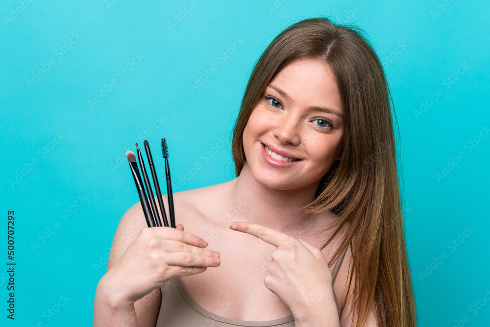 Young caucasian woman isolated on blue background holding makeup brush and pointing it Young caucasian woman isolated on blue background holding makeup brush and pointing it