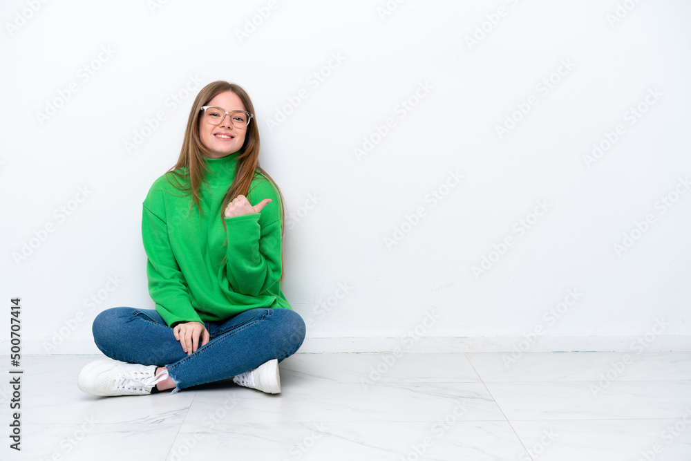 Young caucasian woman sitting on the floor isolated on white background pointing to the side to present a product Young caucasian woman sitting on the floor isolated on white background pointing to the side to present a product