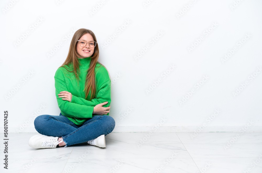 Young caucasian woman sitting on the floor isolated on white background with arms crossed and looking forward Young caucasian woman sitting on the floor isolated on white background with arms crossed and looking forward