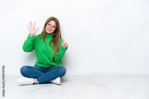 Young caucasian woman sitting on the floor isolated on white background counting six with fingers