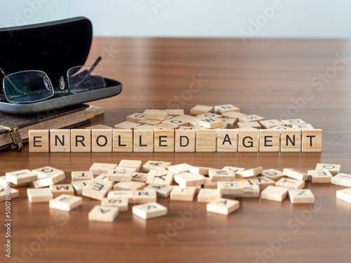 enrolled agent word or concept represented by wooden letter tiles on a wooden table with glasses and a book