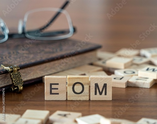 the acronym eom for end of the month word or concept represented by wooden letter tiles on a wooden table with glasses and a book photo