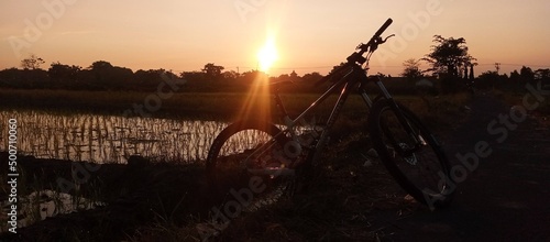 boyolali, central java , indonesia March 17 2022 : morning sky sunrise in the ricefield with sillhouette of a polygon mountain bike and ricefield with blue orange sky photo