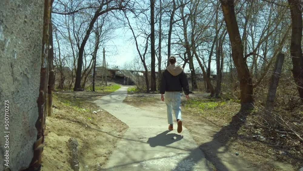 View from behind young woman walking in a poor area on the outskirts of the city on sunny day. Young woman discovering area View from behind young woman walking in a poor area on the outskirts of the city on sunny day. Young woman discovering area