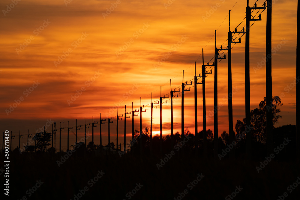 Row High Voltage Power Transmission Pylon lines Against red sunset Sky.