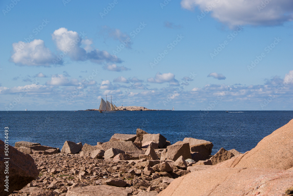 Landscape with a sailing ship on the ocean and red granite rock slabs at Stångehuvud nature reserve in Bohuslän in Sweden.