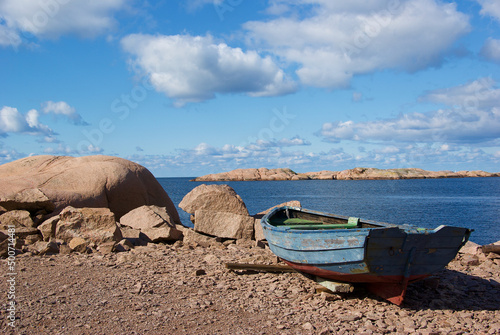 Landscape with ocean and an old worn fishing boat among red granite rock slabs at Stångehuvud nature reserve in Bohuslän in Sweden.