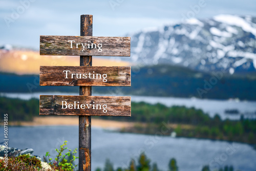 trying trusting believing text quote written on wooden signpost outdoors in nature with lake and mountain scenery in the background фототапет
