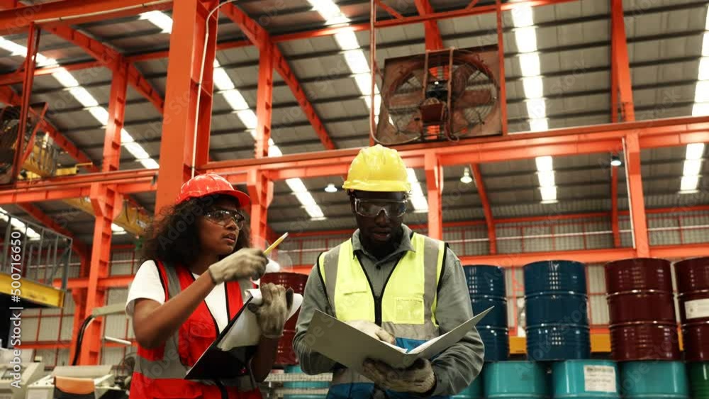 Two engineer worker together, Woman writing on clipboard. Man checking on document folder. Two people wear safety uniform and helmet to work check in factory, Warehouse workshop for factory industrial Two engineer worker together, Woman writing on clipboard. Man checking on document folder. Two people wear safety uniform and helmet to work check in factory, Warehouse workshop for factory industrial