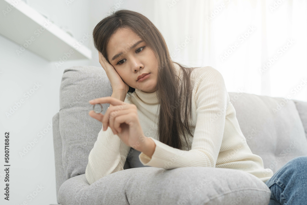 Stressed asian young couple, sad woman quarrel on couch, relationship in trouble. Wife's hand holding wedding ring in disappointment and upset her husband, which may lead to divorce. Problem of family Stressed asian young couple, sad woman quarrel on couch, relationship in trouble. Wife's hand holding wedding ring in disappointment and upset her husband, which may lead to divorce. Problem of family