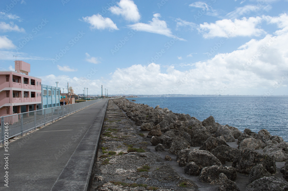 海沿いのカラフルな建物と消波ブロックの並ぶ護岸の遊歩道