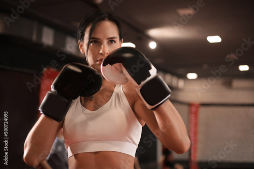 Female in boxing gloves and sportive wear stands in a rack in the boxing hall © ty